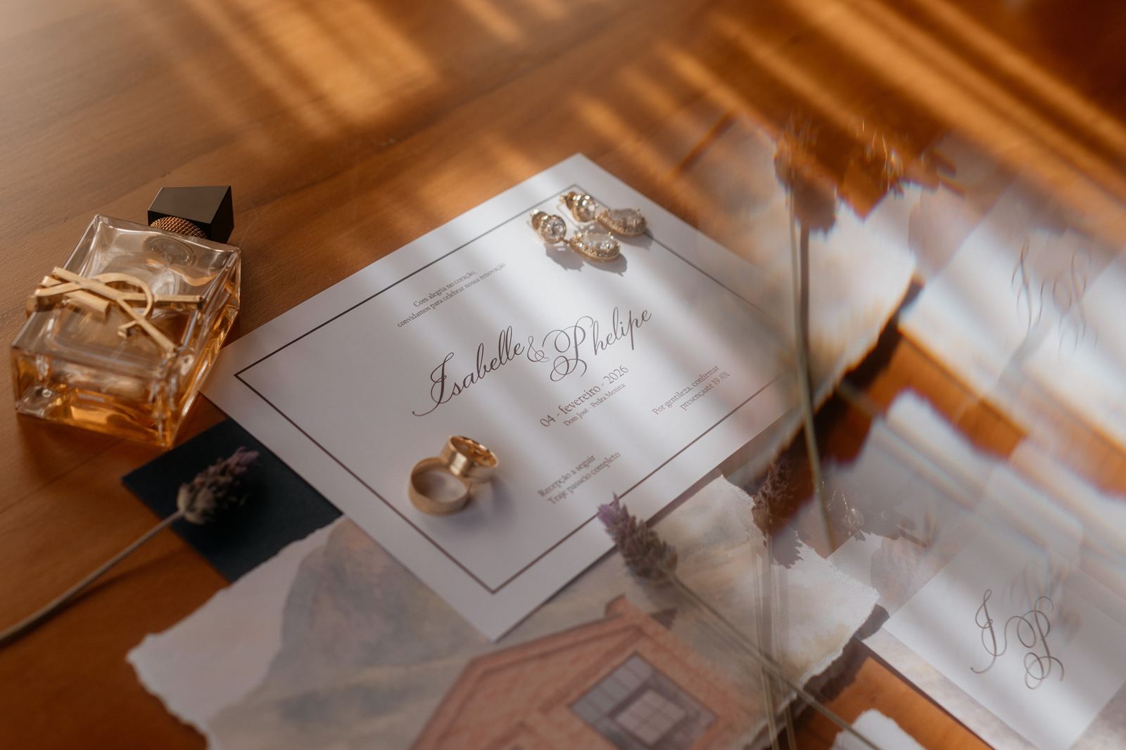 Convite de casamento com alianças, brincos e perfume sobre a mesa